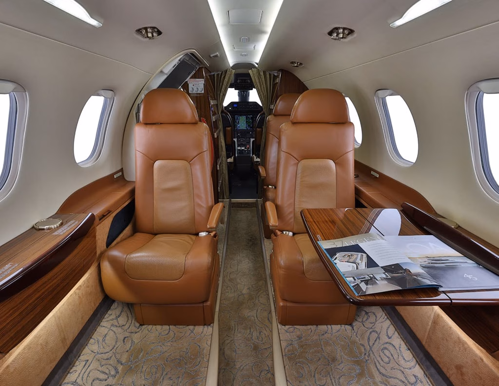 2015 Embraer Phenom 300 cabin looking forward with tan leather seating wood tables and cockpit divider
