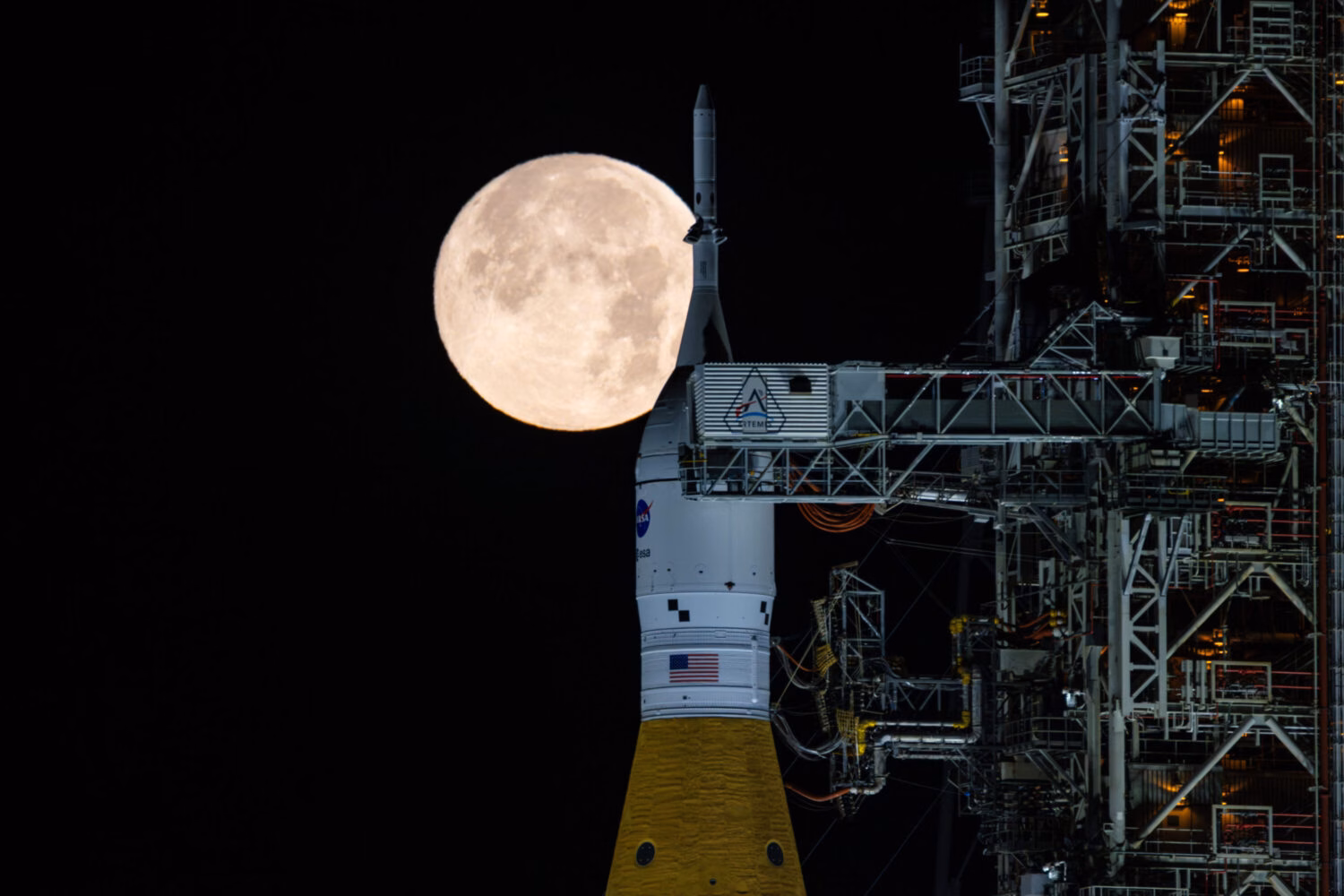 NASA Artemis II SLS rocket and Orion spacecraft on the launch pad at night with the full Moon in the background